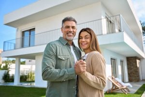 Happy smiling couple and homeowners standing outside their house